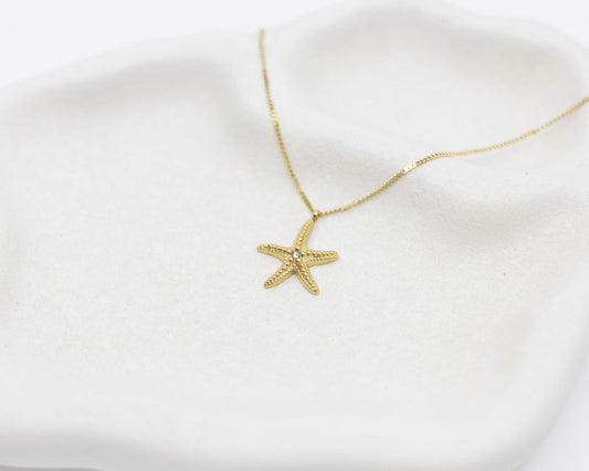 Gold starfish necklace on a white fabric background