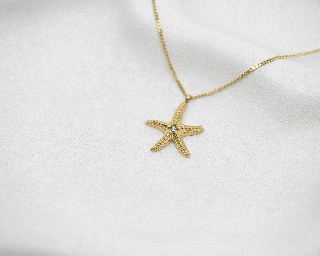 Gold starfish pendant necklace on a white background