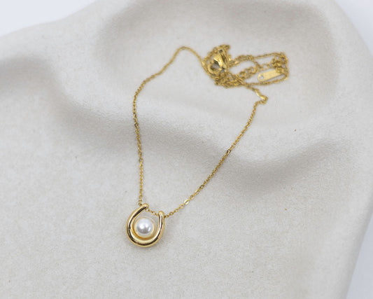 Gold necklace with a pearl pendant on a white surface