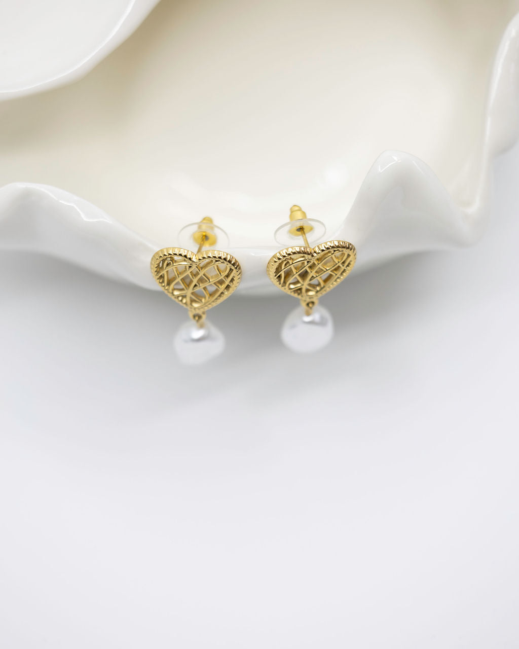 Gold heart-shaped earrings with pearl beads on a white surface