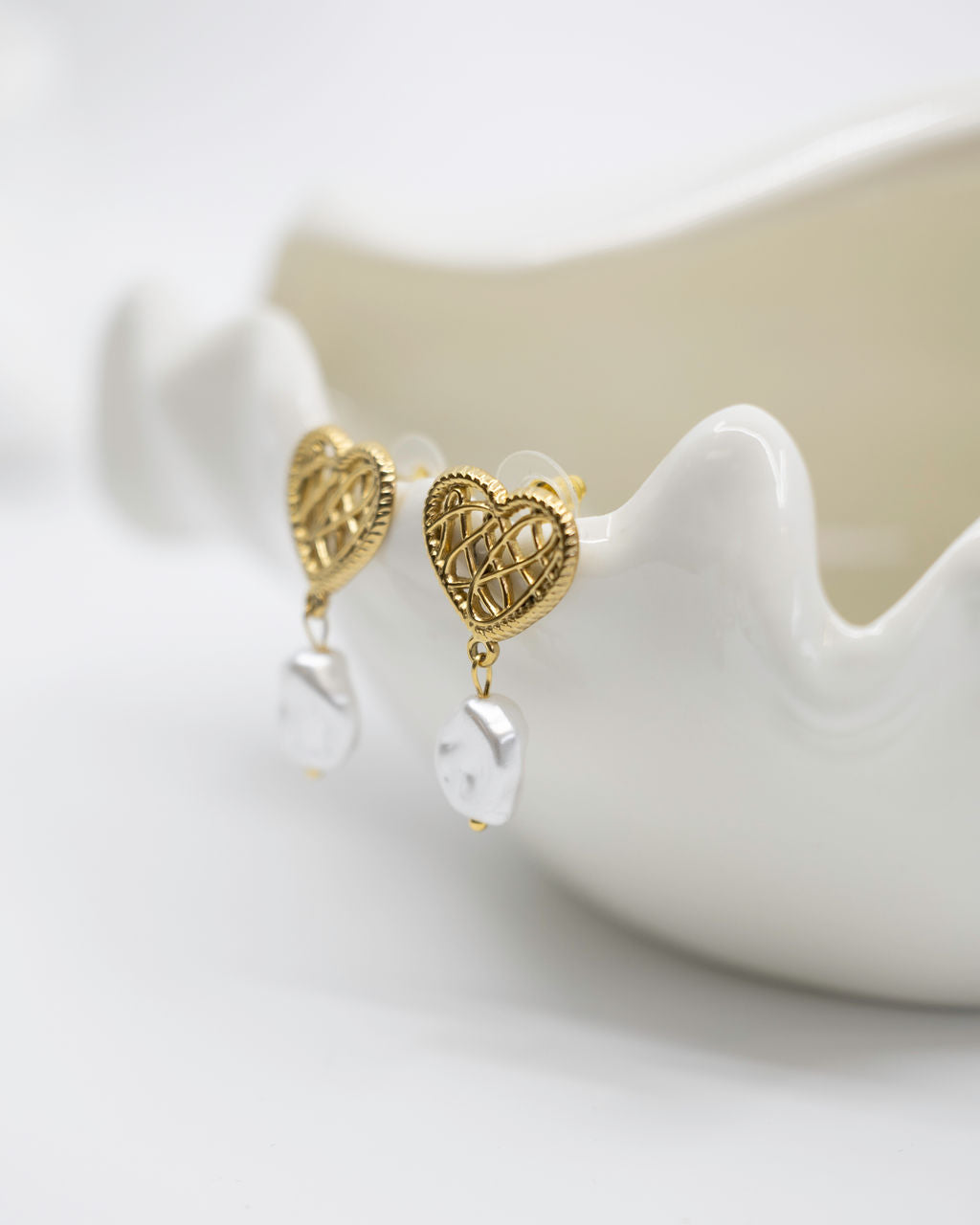 Gold heart-shaped earrings on a white dish with a white background