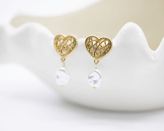 Gold heart-shaped earrings with pearl drops on a white stand.