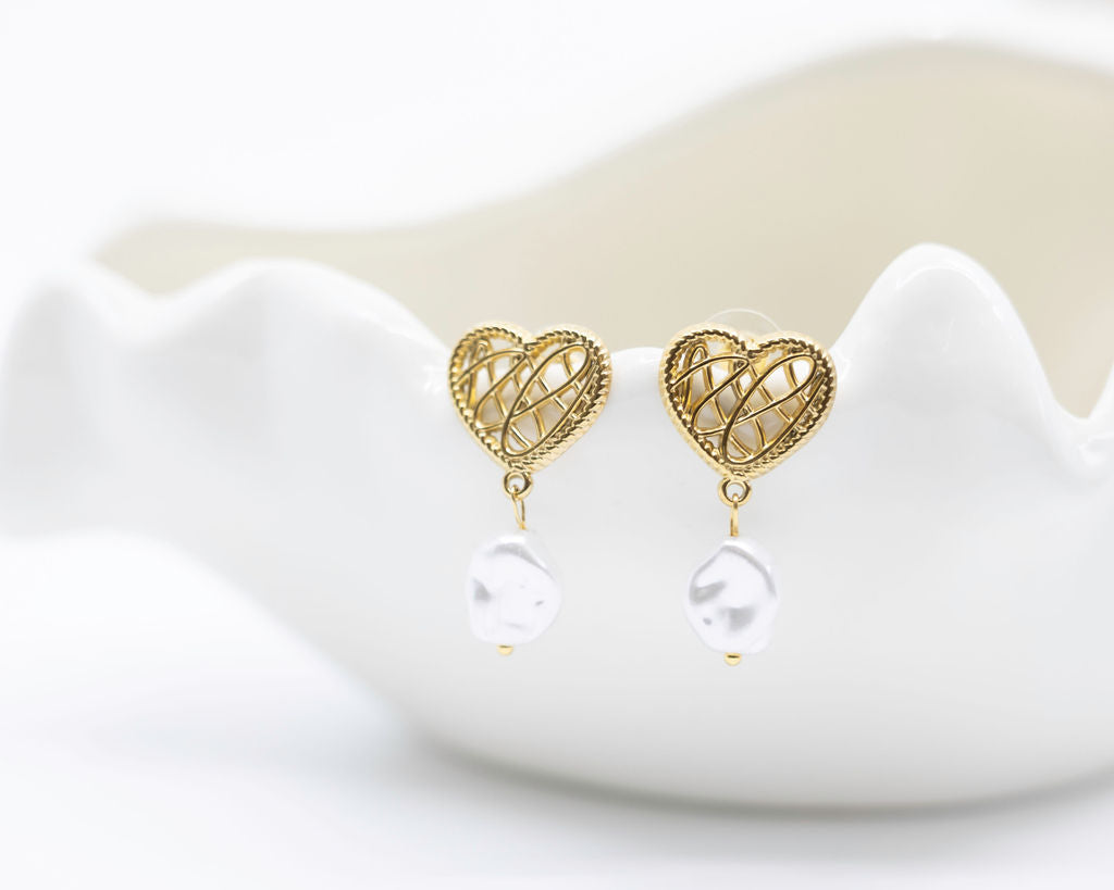 Gold heart-shaped earrings with pearl drops on a white dish