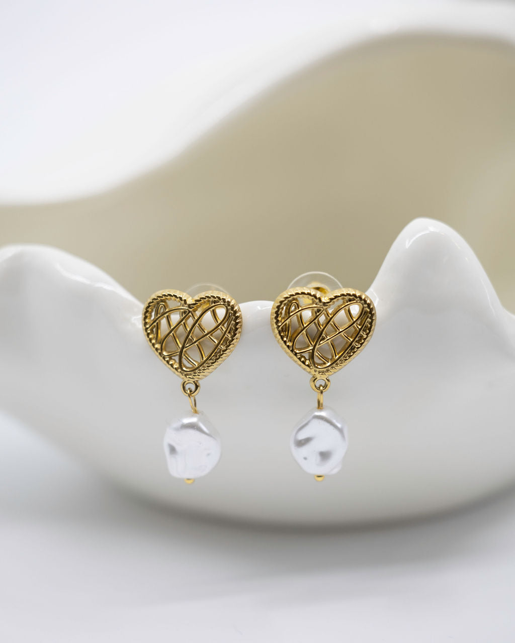 Gold heart-shaped earrings with clear beads on a white dish