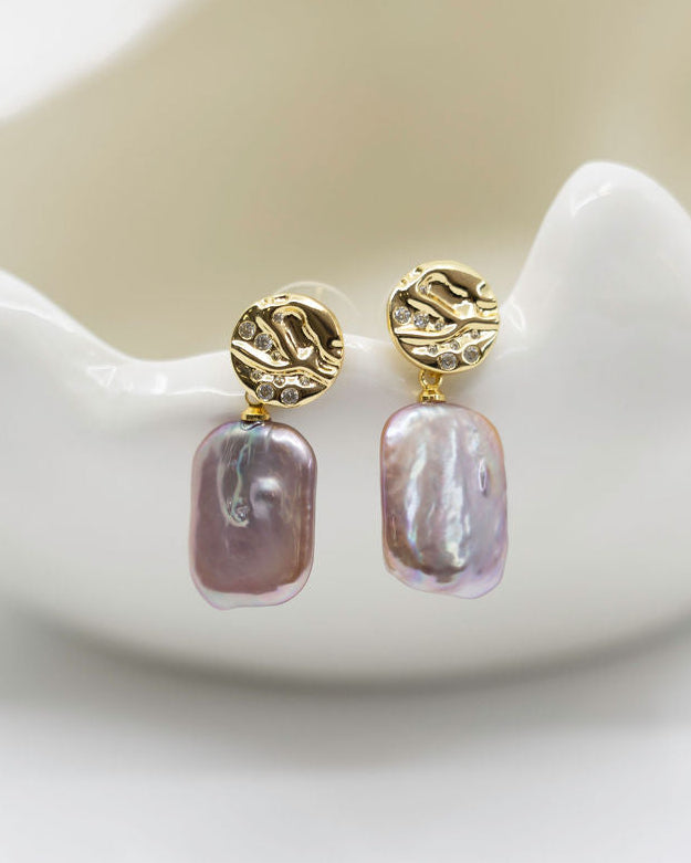 Pair of pearl earrings with gold posts on a white ceramic dish.