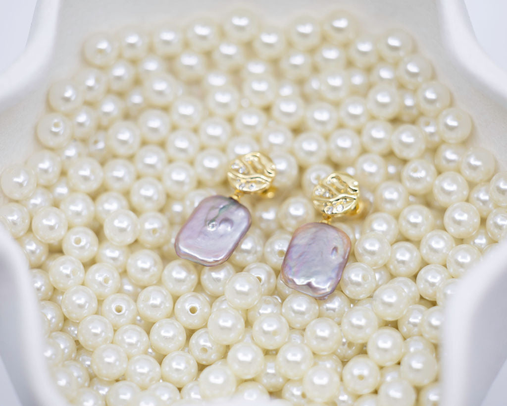 Pearl earrings with gold and purple pearls on a bed of pearls in a white dish.