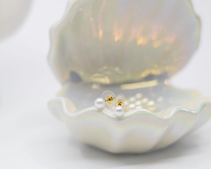 Pearl earrings displayed on a shell with a white background