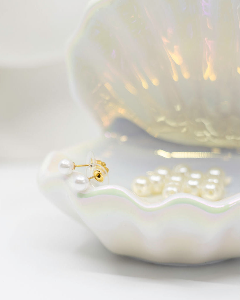 Pearl earrings displayed on a shell with a white background