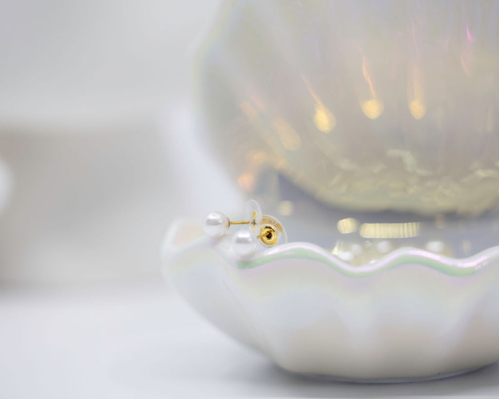 Pearl earrings displayed on a shell with a white background