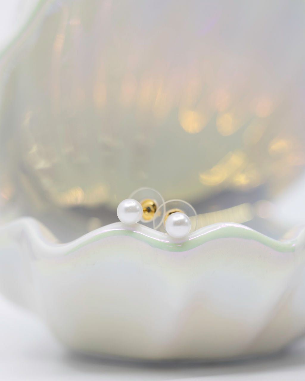 Pearl earrings displayed on a shell with a white background