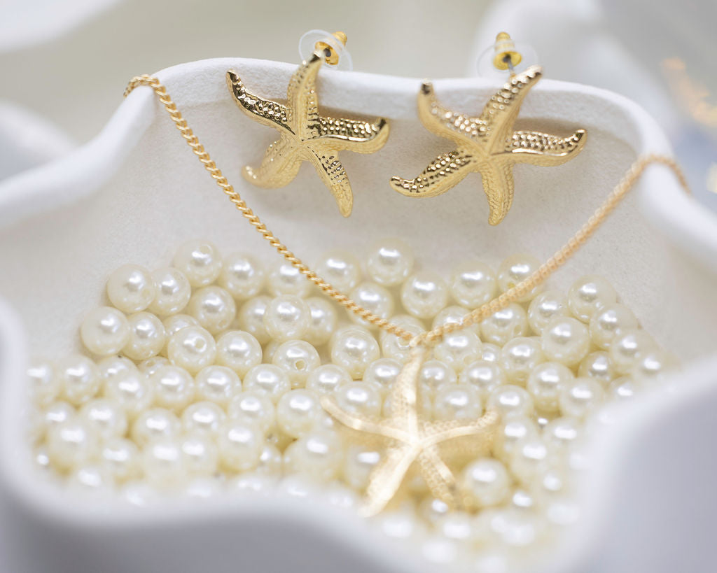 Gold starfish necklace and earrings on a white dish with pearls.