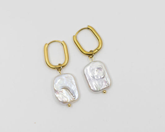 Gold hoop earrings with flat pearls on white background