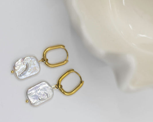 Pair of gold and flat pearl earrings on a white background