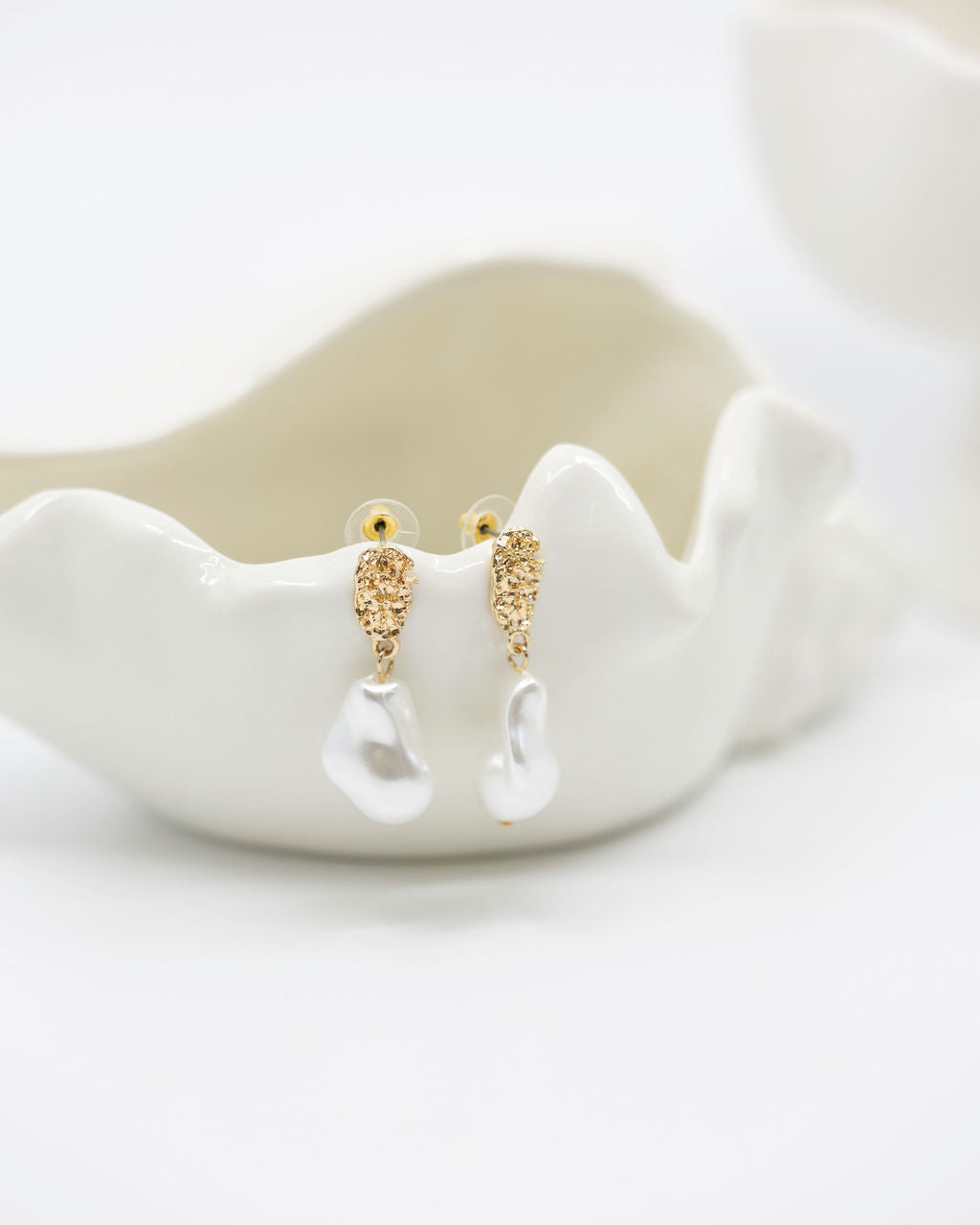 Gold earrings on a white shell