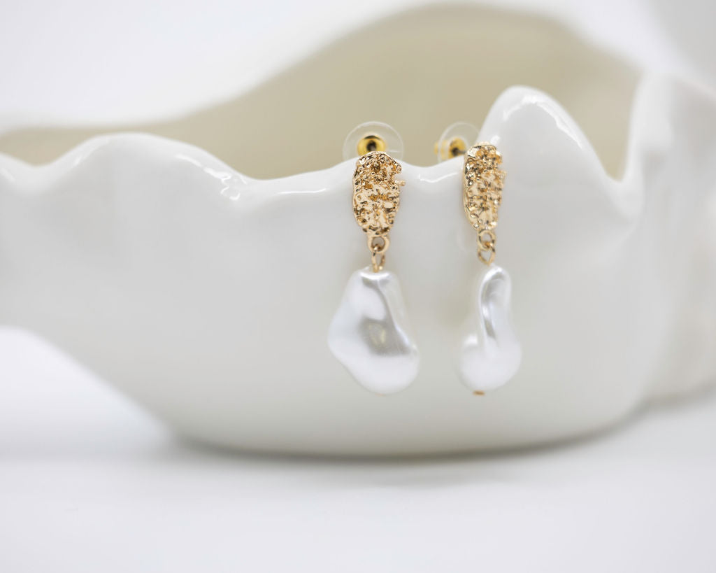 Gold and white earrings on a white ceramic dish