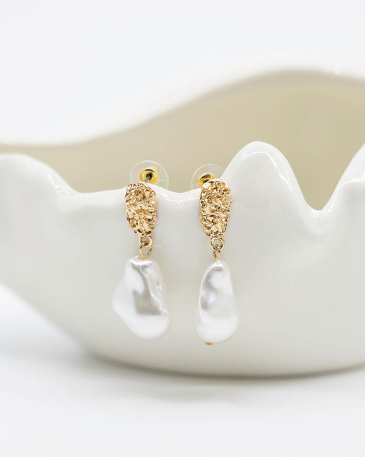 Gold earrings on a white ceramic dish with a plain background