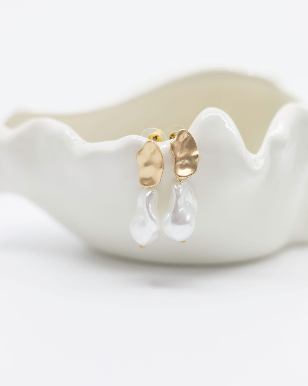 Gold and clear teardrop earrings on a white ceramic dish