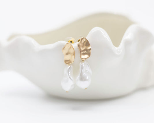 Gold earrings with clear drops on a white ceramic dish