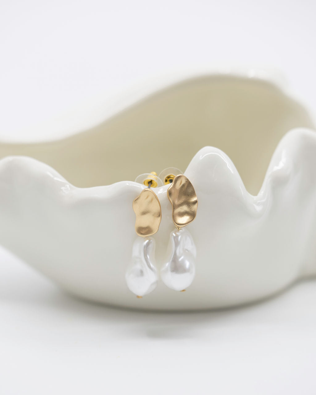Gold and clear earrings on a white ceramic dish with a white background