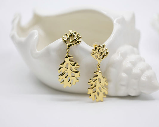 Gold coral-shaped earrings on a white ceramic dish