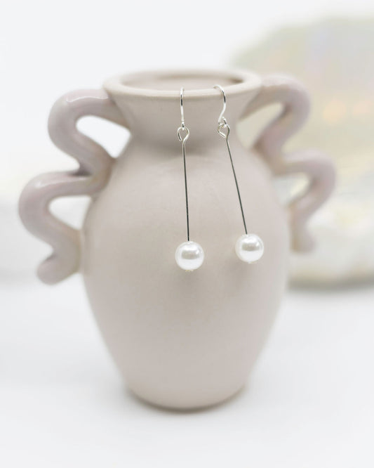 Pearl earrings hanging from a ceramic vase on a light background
