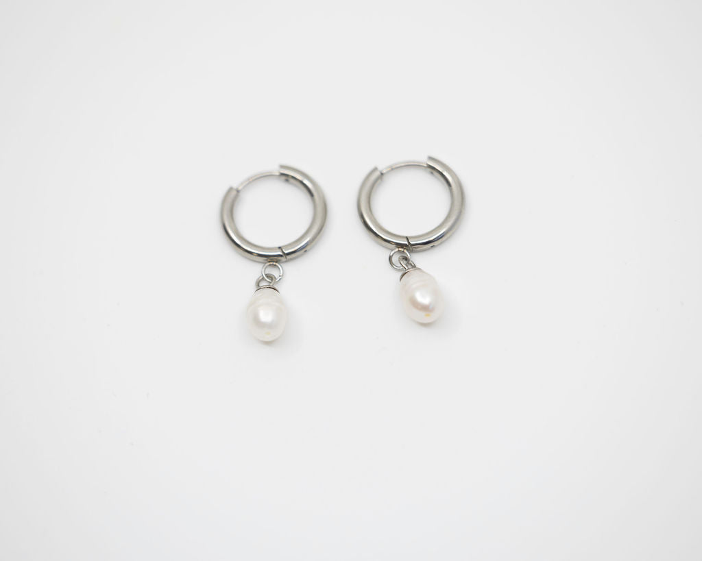 Pair of silver hoop earrings with pearl charms on a white background