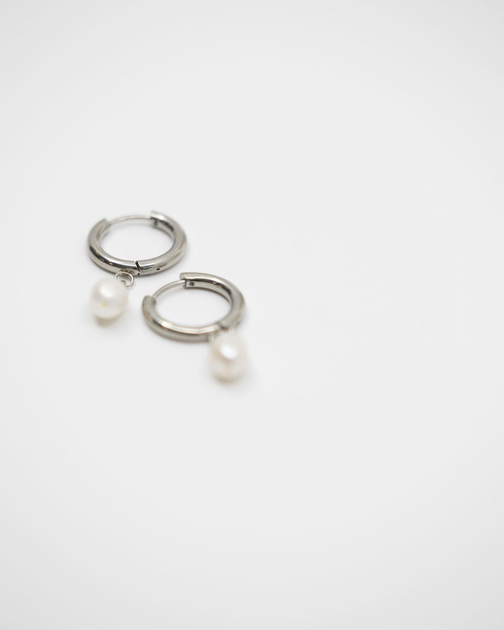 Pair of silver hoop earrings with pearls on a white background