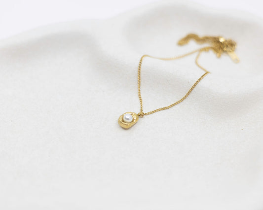 Gold necklace with a pearl pendant on a white background