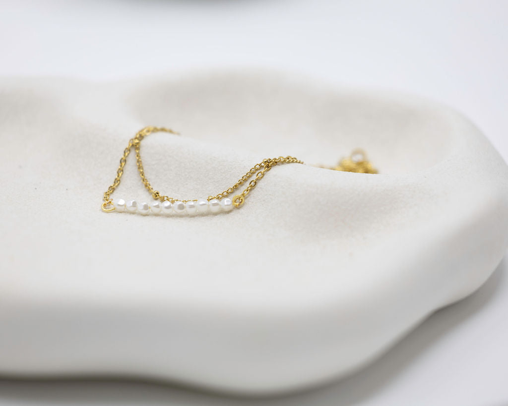 Gold necklace with pearls on a white ceramic dish