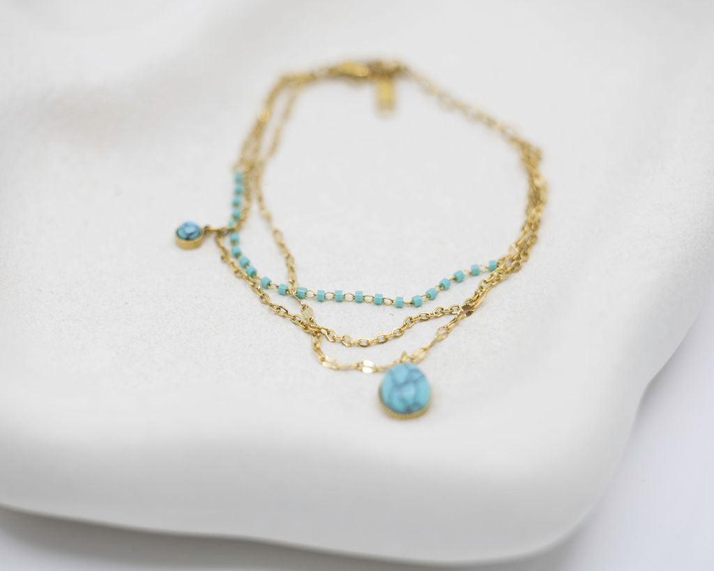 Two gold necklaces with turquoise beads on a white surface