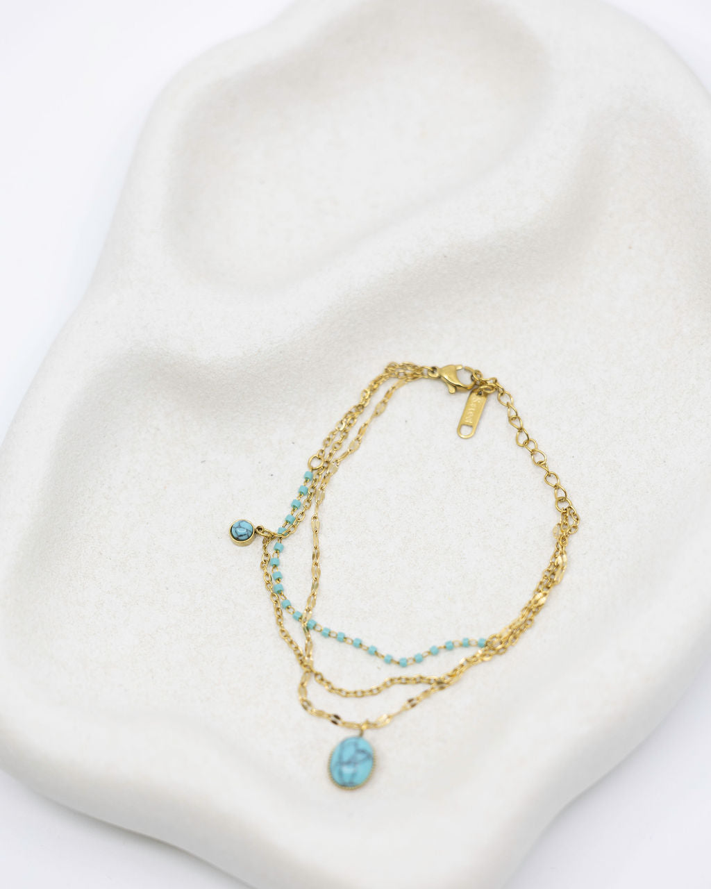 Gold bracelet with turquoise stones on a white heart-shaped pillow