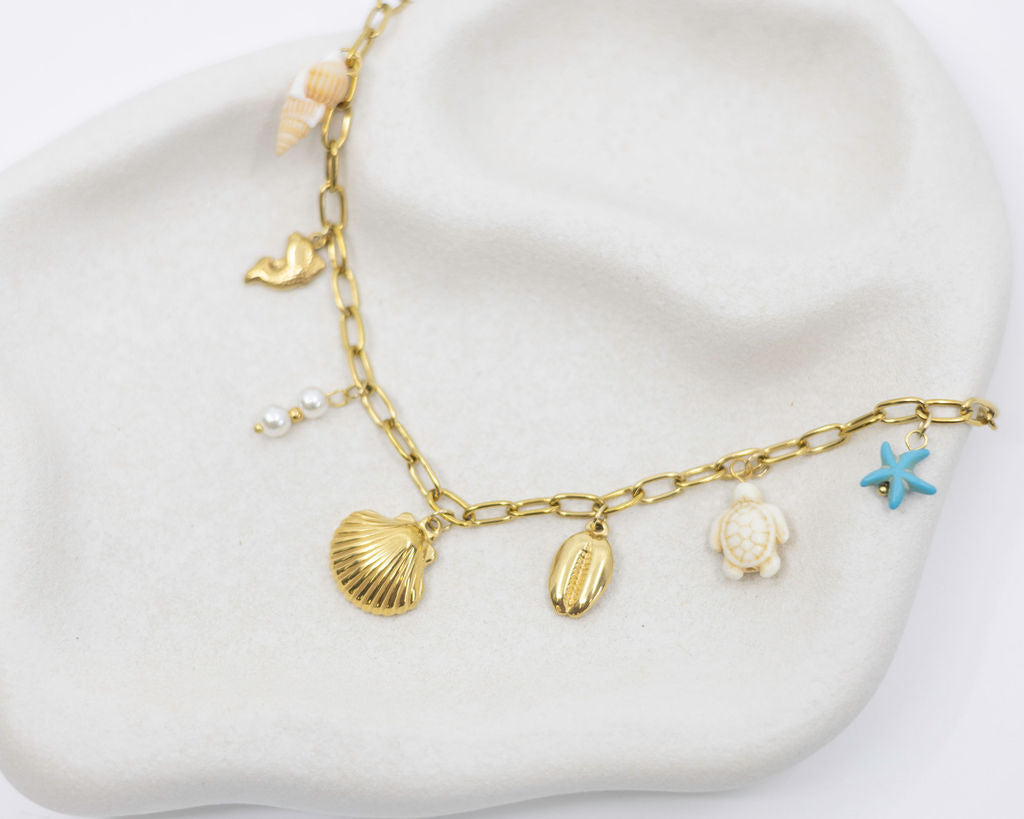 Gold necklace with shell and starfish charms on a white surface