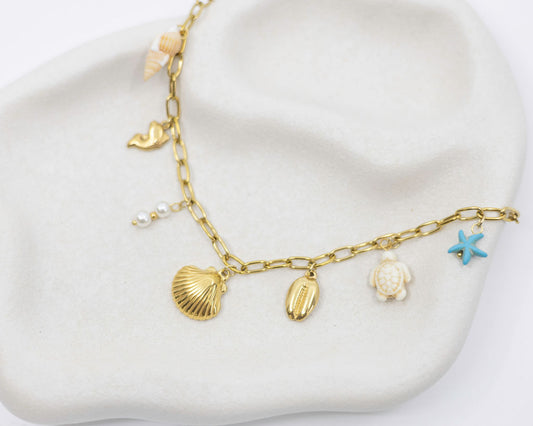 Gold necklace with shell and starfish charms on a white surface