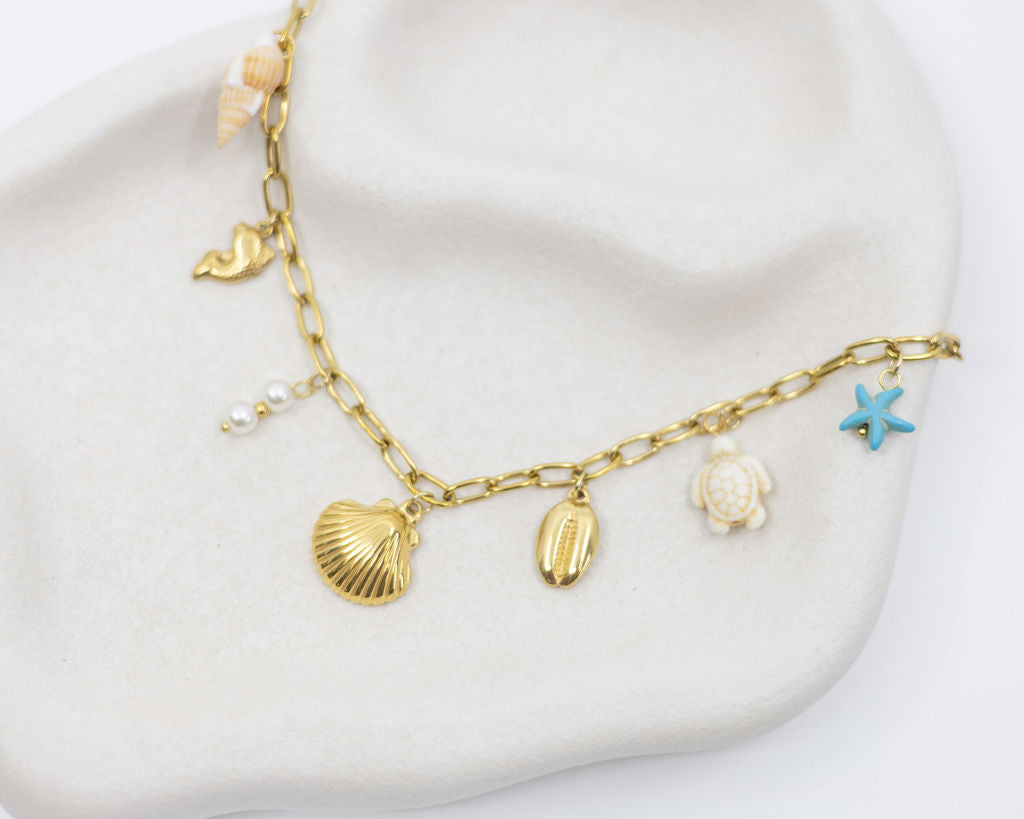 Gold necklace with shell and starfish charms on a white surface