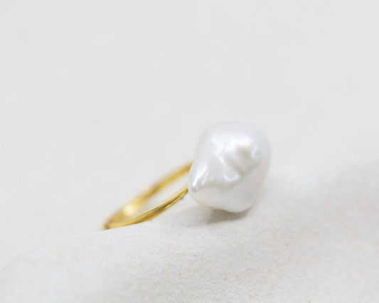 Pearl ring with gold band on a light gray background