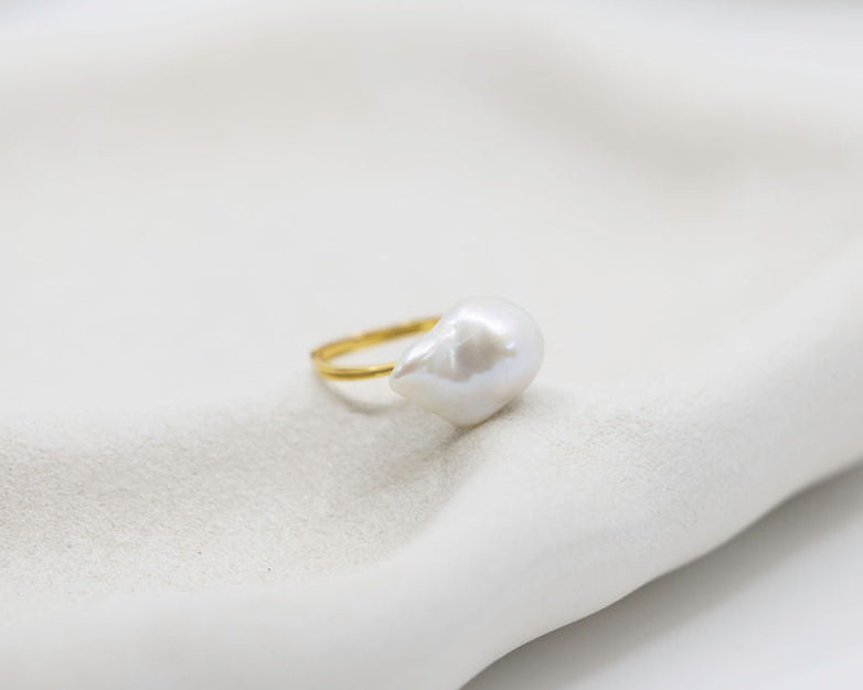 Gold ring with a white pearl on a light grey background