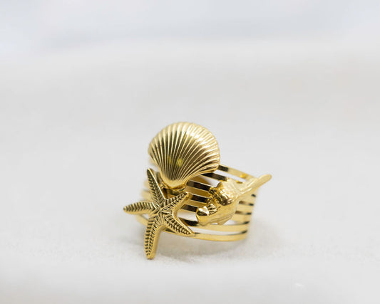 Gold ring with shell and starfish design on a white background