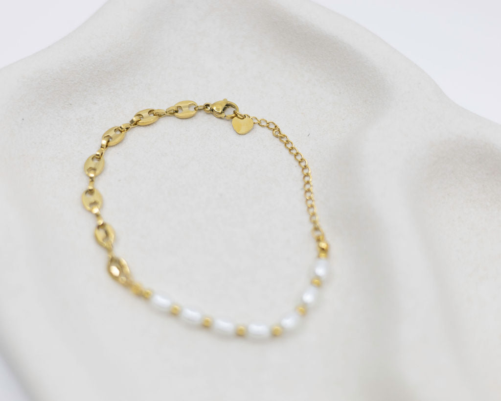 Gold bracelet with white beads on a light gray background
