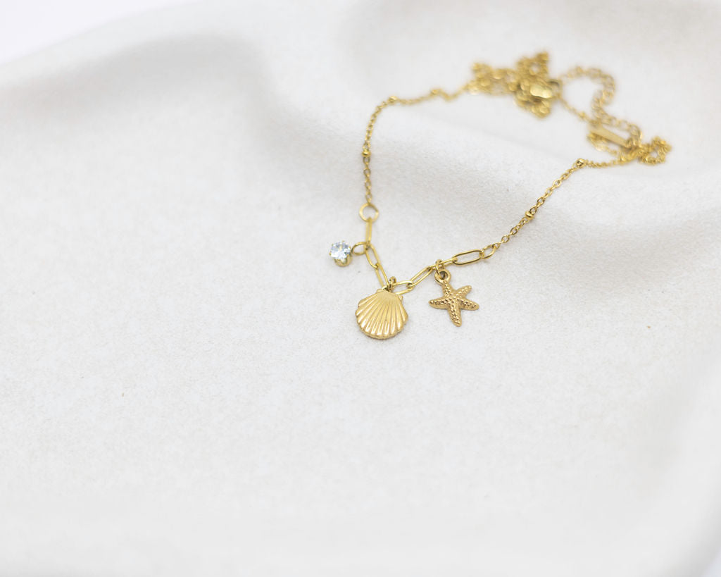 Gold bracelet with shell and starfish charms on a white background