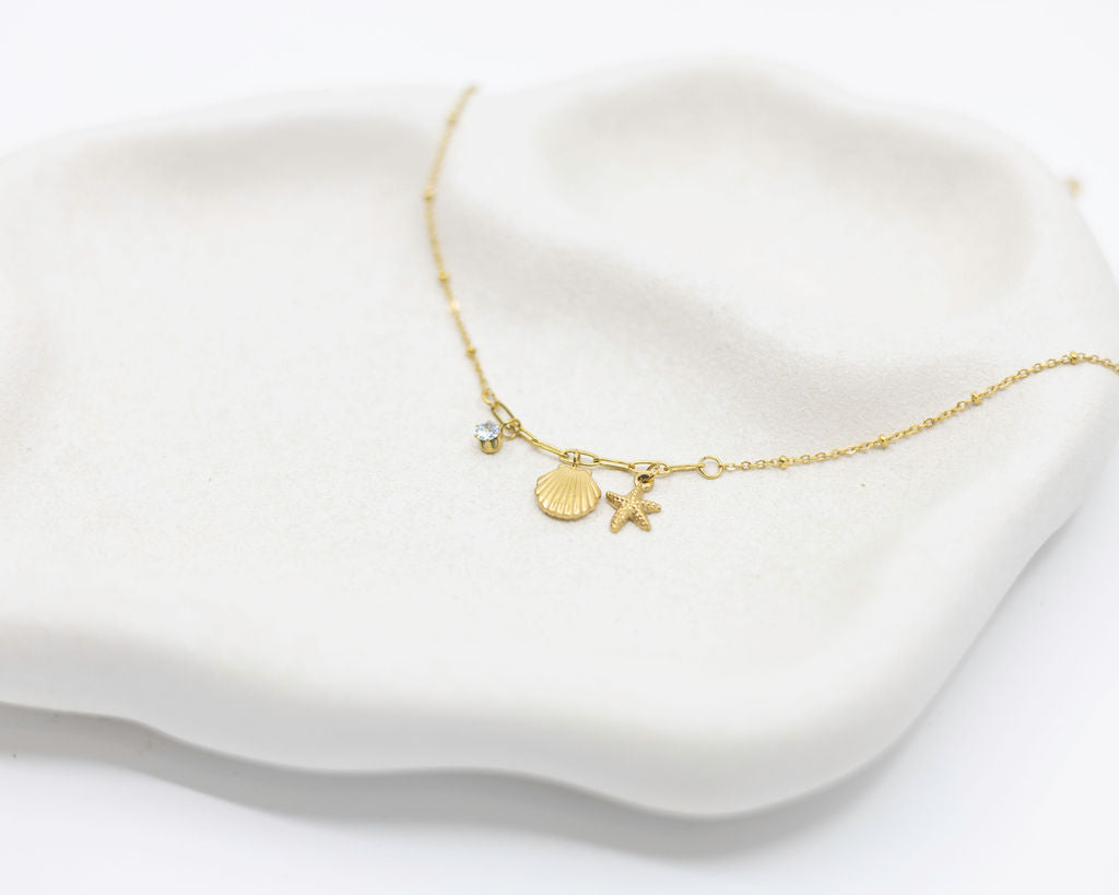 Gold bracelet with shell and star charms on a white fabric background