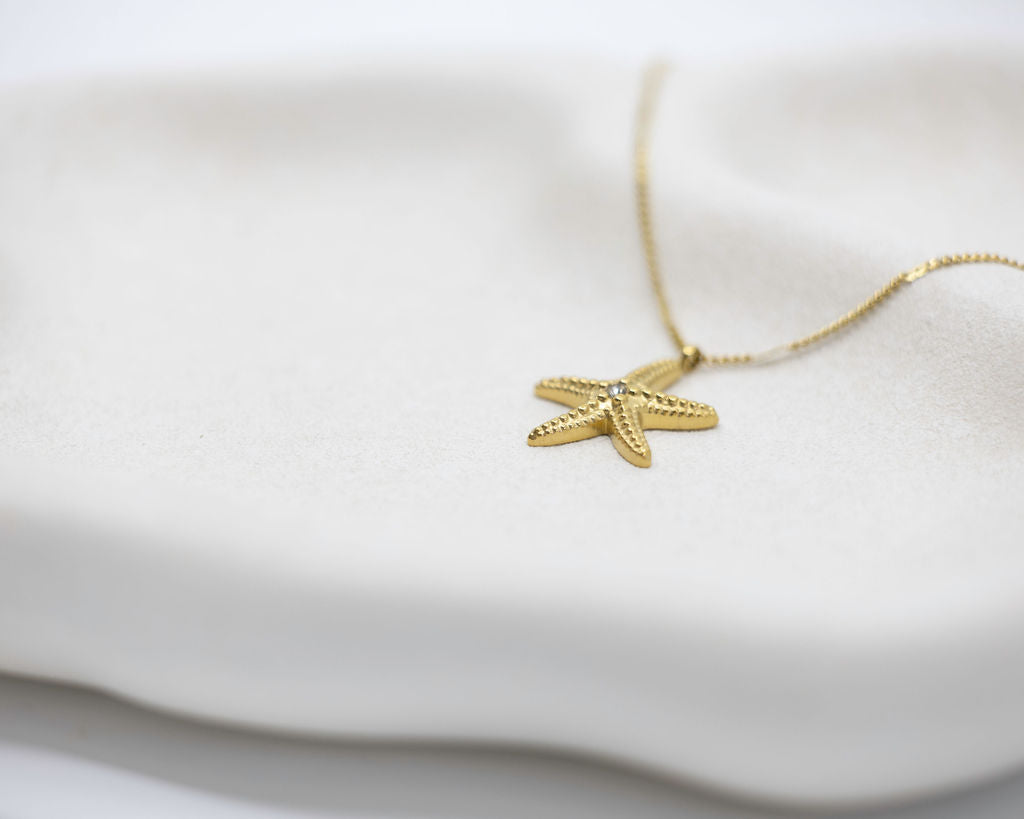 Gold starfish pendant necklace on a white fabric background