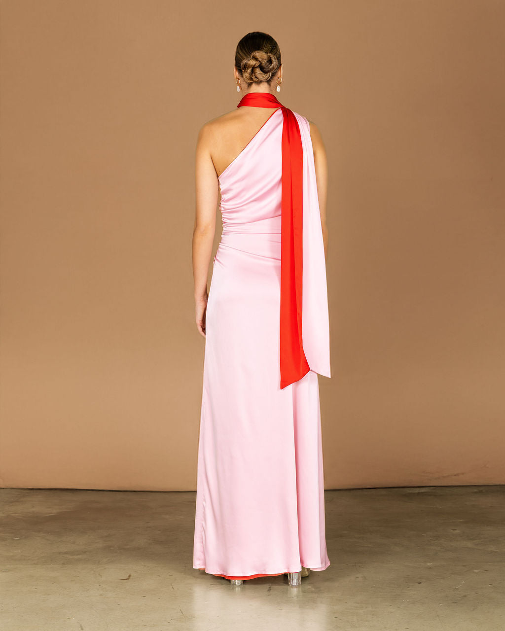 Woman wearing a pink one-shoulder dress with a red sash on a beige background
