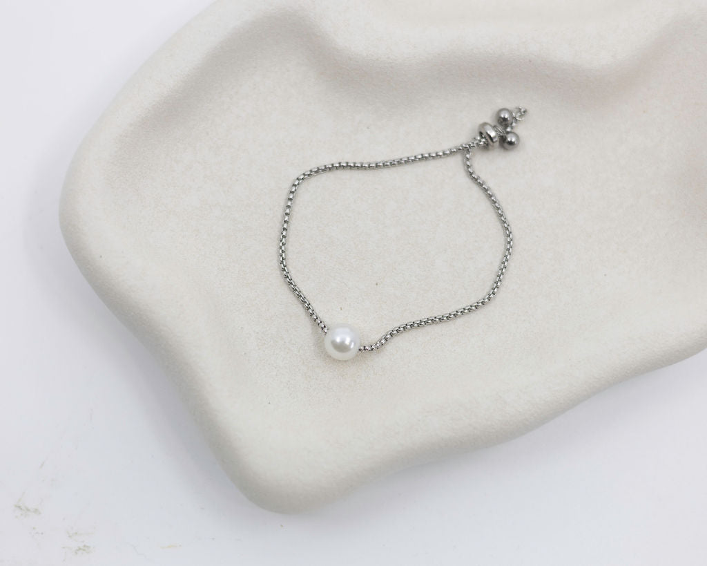 Silver bracelet with a pearl on a beige fabric background